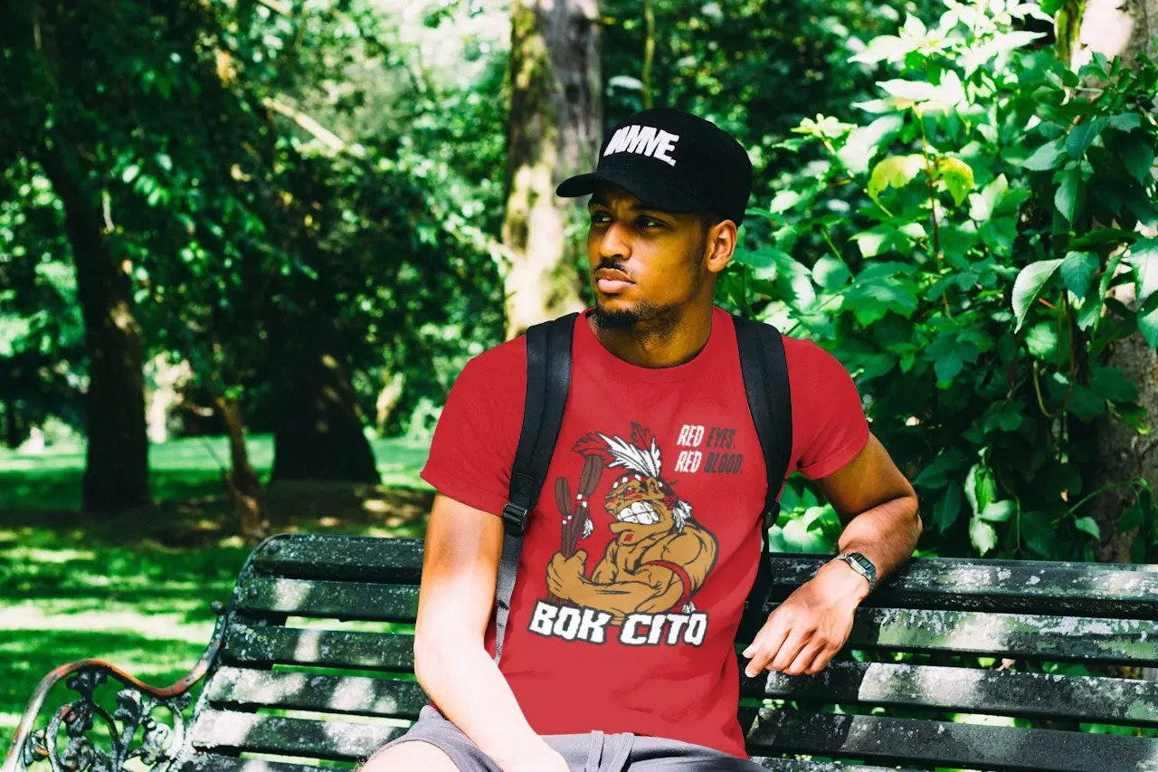 Man wearing a hat and Bok Cito fan shirt while sitting on a bench